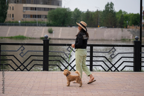 A beautiful Asian girl (Kazakh) walks with her dog (mini poodle). Summer portrait of a young woman in the park.