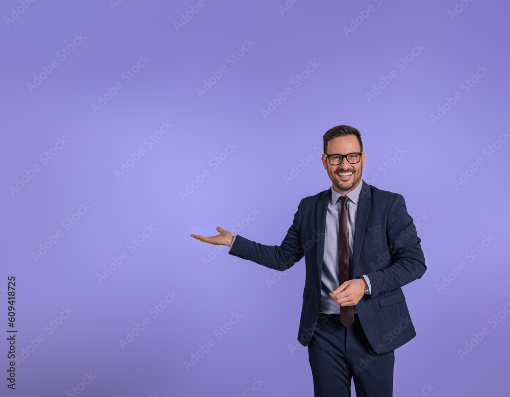 Portrait of smiling handsome marketing manager showing copy space for business advertisement. Happy male entrepreneur presenting and recommending new product while standing isolated on blue background Portrait of smiling handsome marketing manager showing copy space for business advertisement. Happy male entrepreneur presenting and recommending new product while standing isolated on blue background