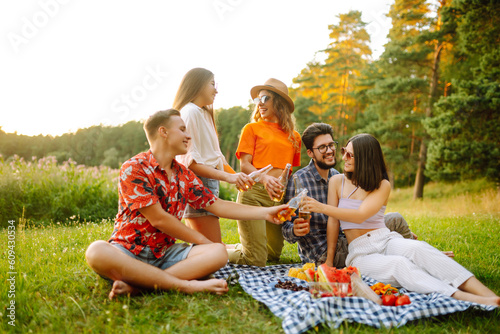 Group of happy friends cheers and drink beers on in summer park. Vacation, picnic, friendship or holliday concept.
