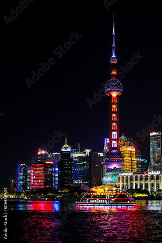 Tour boat cruises along the Huangpu River passing the iconic Oriental Pearl Tower and other colourful buildings lighting up the Shanghai night cityscape