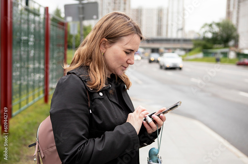 Free Download a young woman stands on the street of a big city with a mobile phone in her hands - GFXLoad