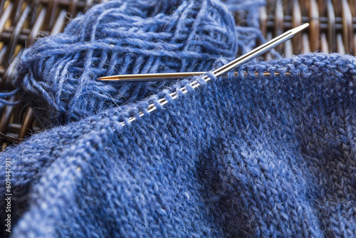 Blue wool yarn knitting on the metal needles with yarn ball, stockinette stitch knitted texture in progress close-up photo
