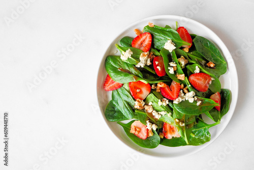 Summer salad of spinach, strawberries and blue cheese. Overhead view on a white marble background.