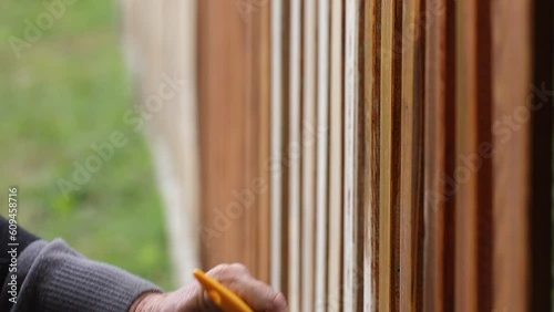 Painting protective varnish on wooden picket fence at backyard. Motion of hand with paintbrush. Handheld shot photo