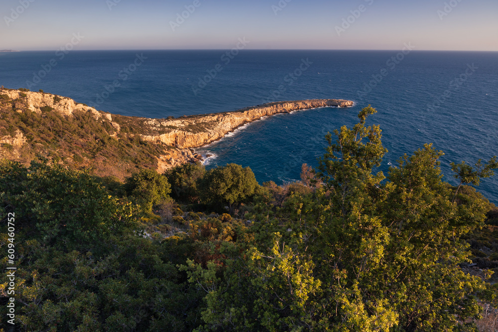 Sunset seascape with bright lit long narrow cape and dense forest in foreground, Lycian Way, Turkey