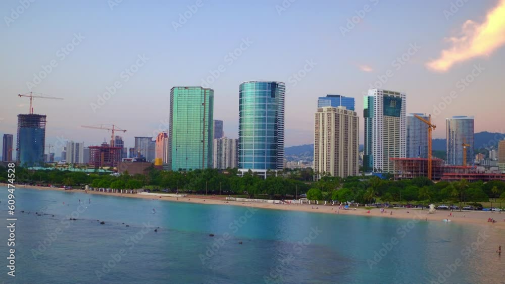 Aerial Shot Of Modern Skyscrapers Near People At Beach, Drone Flying Forward Over Sea Against Sky At Sunset - Oahu, Hawaii Aerial Shot Of Modern Skyscrapers Near People At Beach, Drone Flying Forward Over Sea Against Sky At Sunset - Oahu, Hawaii