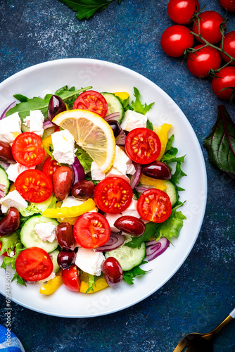 Tasty Greek salad with feta cheese, kalamata olives, tomatoes, paprika, cucumber and onion, healthy mediterranean food. Blue table background, top view