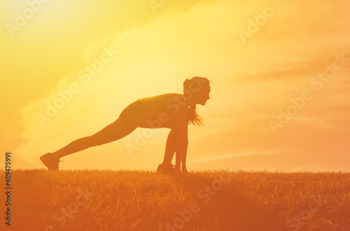 Female runner stretches doing exercise at sunset 