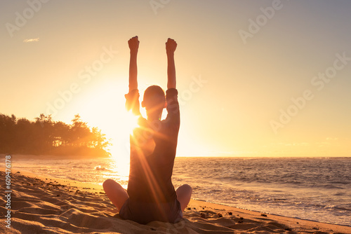 Fototapeta Young woman sitting on a beach feeling strong inspired energized facing the sunr