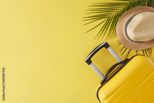 The idea of a sunny vacation. Top view flat lay of yellow suitcase, straw hat, palm leaves on yellow background with empty space for text or promotions