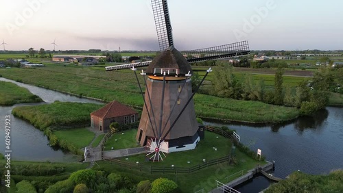 Spectaculair aerial footage of a classic Dutch windmill surrounded by water in the evening hours. Extreme high angle view.