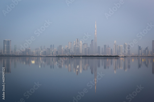 Dubai Downtown skyline panorama with reflections in Dubai Creek, cold colors, seen from Dubai Creek Harbour promenade before sunrise.