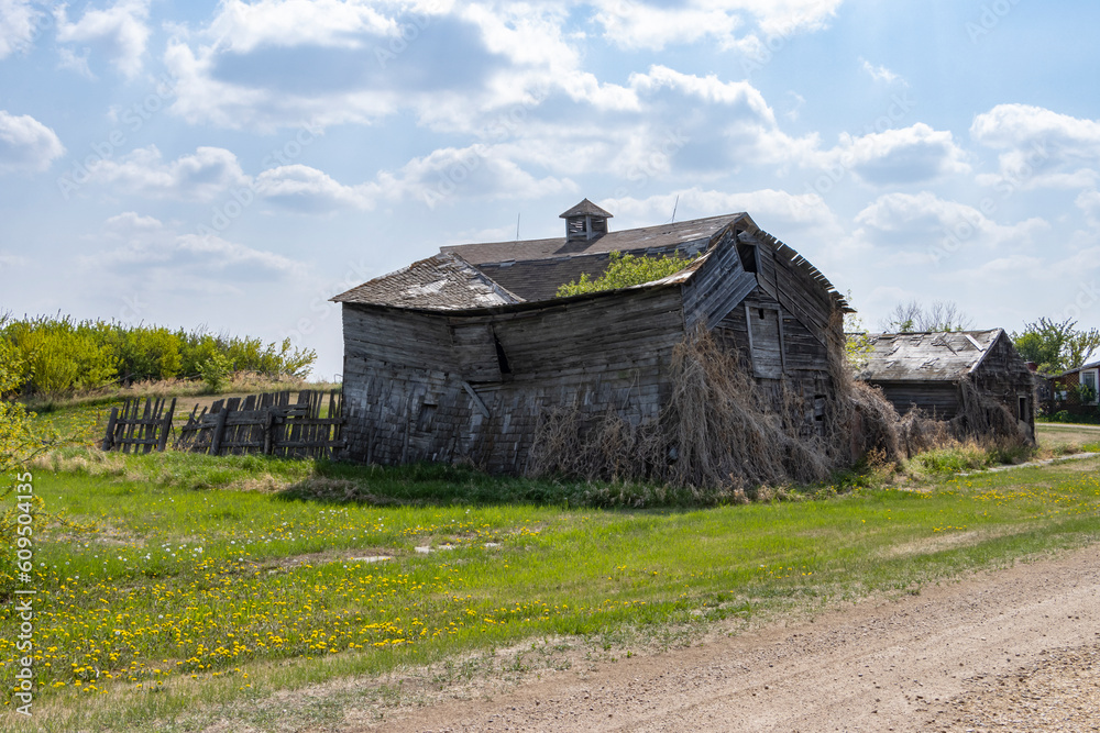 old abandoned barn in the countryside falling down, crumbling, with blue cloudy sky and green grass surrounding it old abandoned barn in the countryside falling down, crumbling, with blue cloudy sky and green grass surrounding it