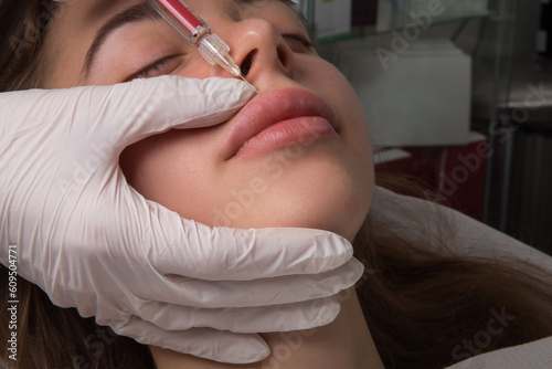 Close up of hands of cosmetologist making botox injection in female lips. She is holding syringe. The young beautiful woman is receiving procedure with enjoyment
