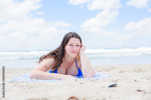 ビーチでタオルの上に寝そべりカメラを見つめる水着の白人女性