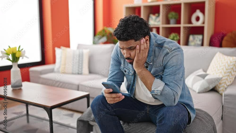 African american man using smartphone with worried expression at home African american man using smartphone with worried expression at home