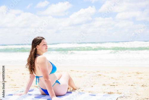 ビーチに座り振り返るビキニを着た白人女性と綺麗な海