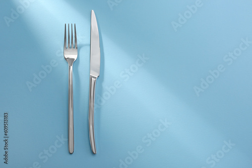 Shiny fork and knife on light blue background  flat lay. Space for text