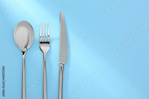 Spoon  fork and knife on light blue  flat lay. Space for text