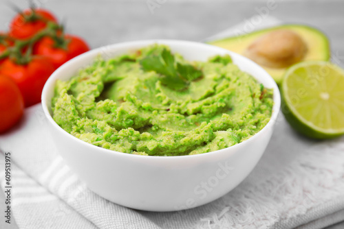 Bowl of delicious guacamole and ingredients on cloth, closeup