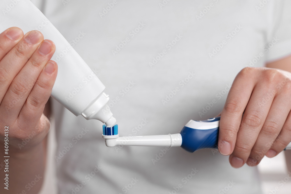 Woman squeezing toothpaste from tube onto electric toothbrush, closeup Woman squeezing toothpaste from tube onto electric toothbrush, closeup