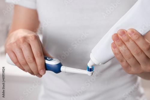 Woman squeezing toothpaste from tube onto electric toothbrush, closeup