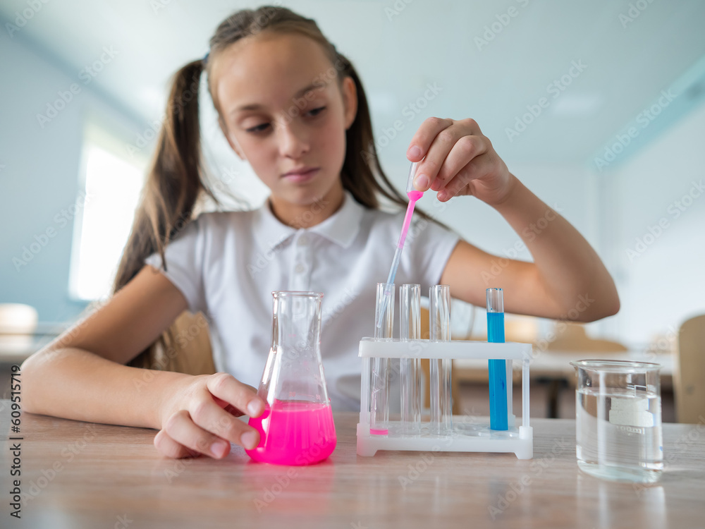A schoolgirl conducts experiments in a chemistry lesson. Girl pouring colored liquids from a beaker. A schoolgirl conducts experiments in a chemistry lesson. Girl pouring colored liquids from a beaker.