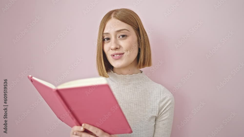 Young blonde woman smiling confident reading book doing thumb up gesture over isolated pink background Young blonde woman smiling confident reading book doing thumb up gesture over isolated pink background