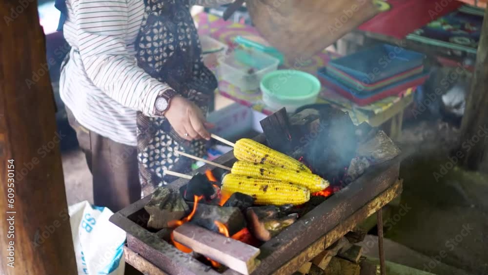 close up of woman hands roasting sweet corn while fanning, with charcoal fire and blurred background close up of woman hands roasting sweet corn while fanning, with charcoal fire and blurred background