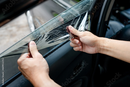 Car side window film removal and tinting installation. Male auto specialist worker hand gently carefully peeling off the old protective car film from glass surface.