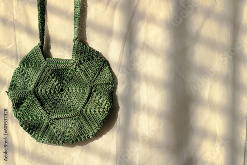 handmade olive green yarn crochet hexagon shape creative bag on white background with sunlight. copy space for text.