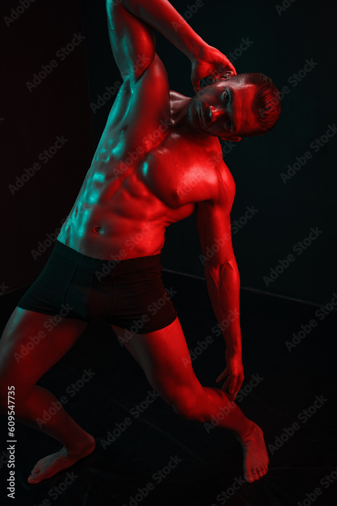 Man bodybuilder athlete with bare torso fashion pose on black isolated background with colored light neon red and green. The concept of a healthy male body sport