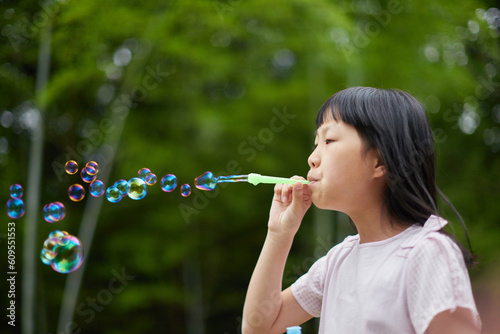 夏の公園でシャボン玉を遊ぶ可愛い小学生の女の子の様子