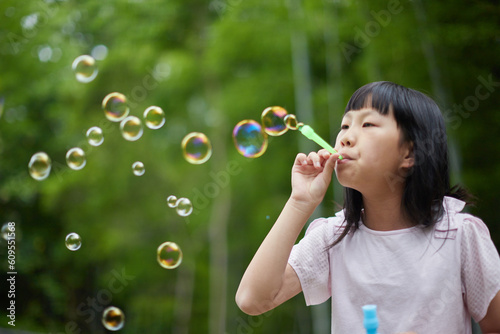 夏の公園でシャボン玉を遊ぶ可愛い小学生の女の子の様子