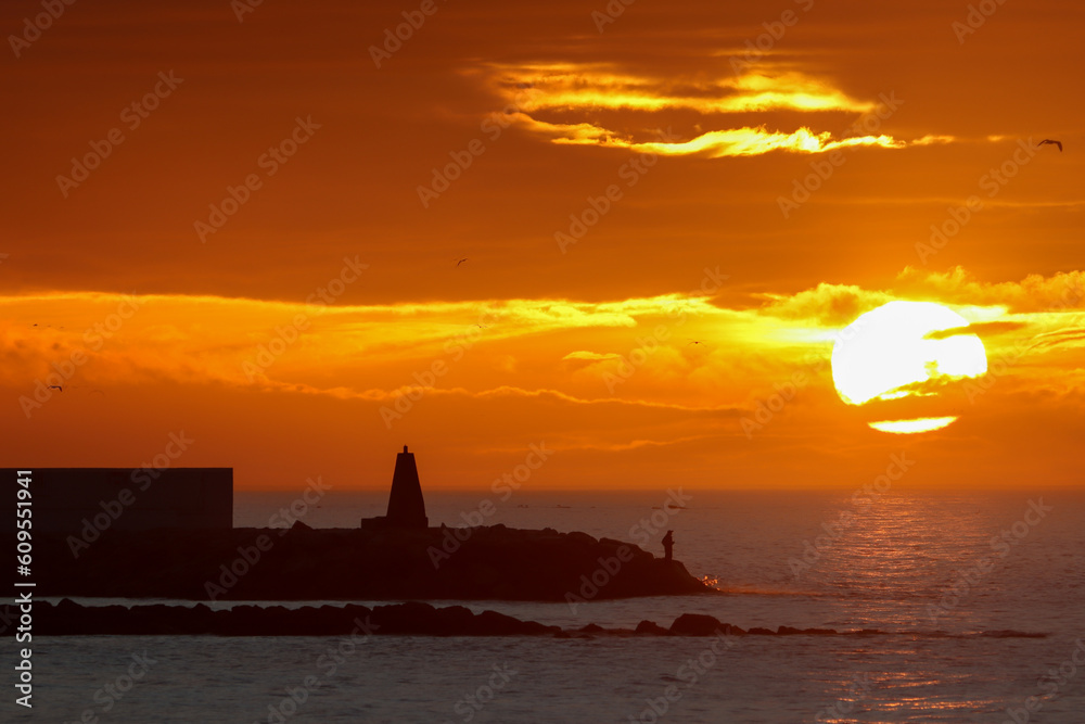 golden yellow sunrise with a fisherman and cairn and the sun rising behind the clouds