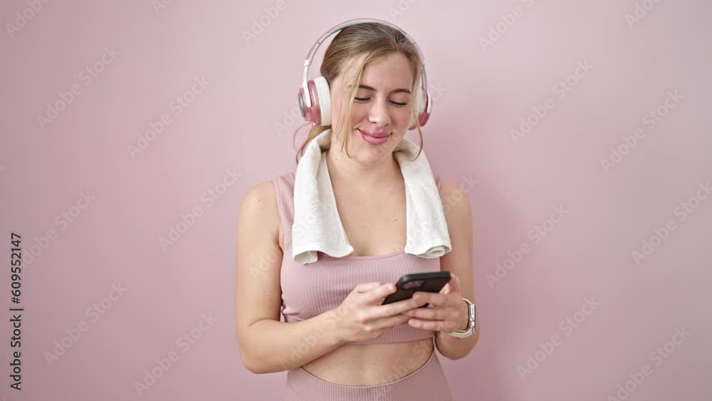 Young blonde woman wearing sportswear using smartphone and headphones over isolated pink background Young blonde woman wearing sportswear using smartphone and headphones over isolated pink background