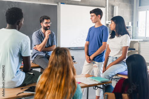 Group of teenagers and male teacher at classroom talking and discussing together photo