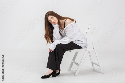 girl model in white shirt and black trousers sits relaxed in studio