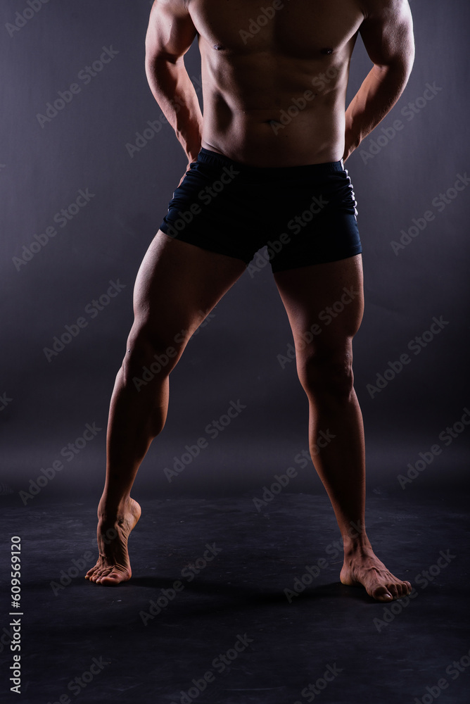 Muscular male legs, man in studio, dark background