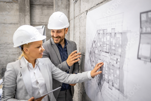 Structural engineers with project plan and tablet computer controlling and inspecting building process.