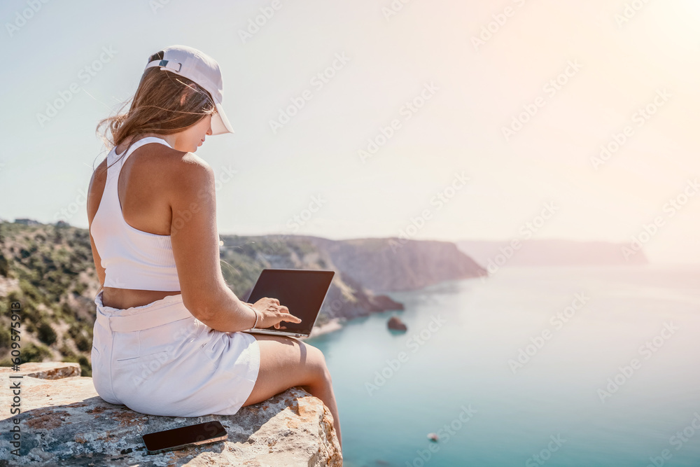 Digital nomad, Business woman working on laptop by the sea. Pretty lady typing on computer by the sea at sunset, makes a business transaction online from a distance. Freelance, remote work on vacation