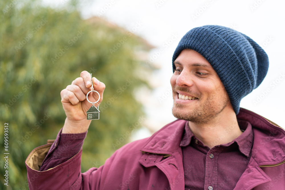 Fototapeta premium Young caucasian man holding home keys at outdoors