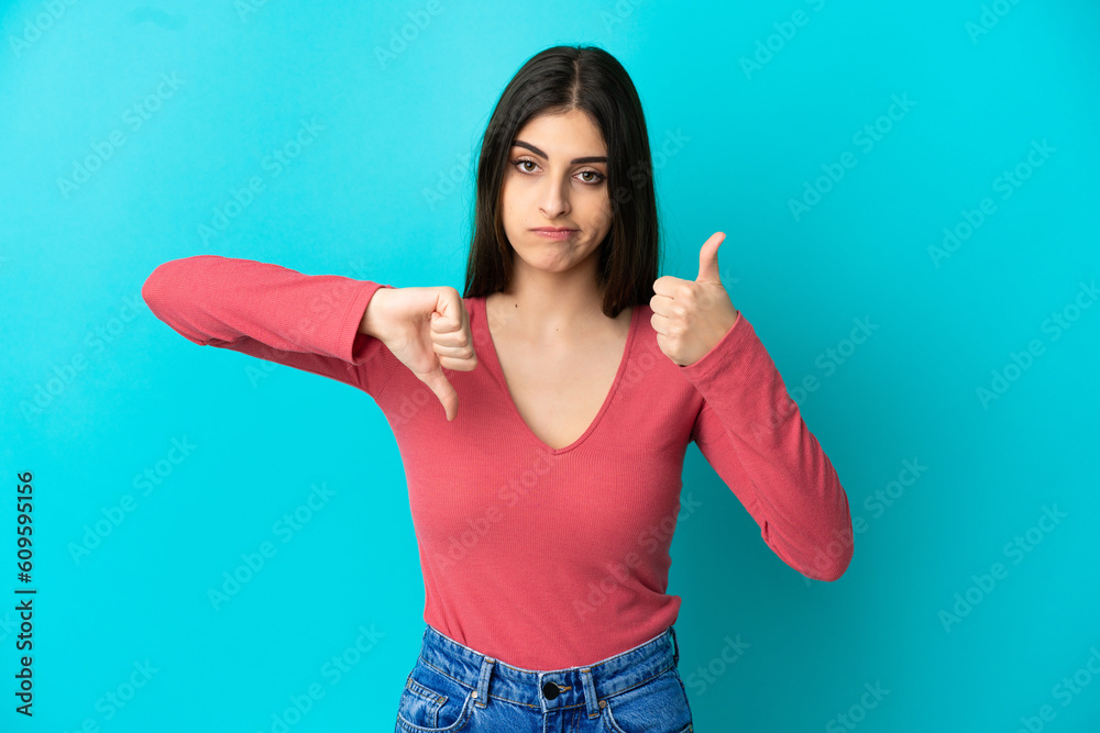 Fototapeta premium Young caucasian woman isolated on blue background making good-bad sign. Undecided between yes or not