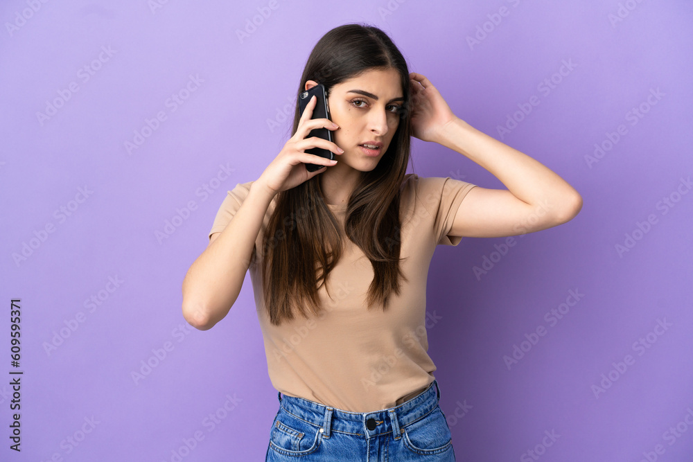Young caucasian woman using mobile phone isolated on purple background having doubts