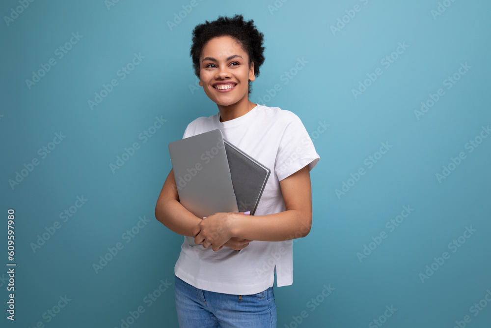 young latin brunette female student in a white t-shirt holding a laptop and working notebooks in her hands young latin brunette female student in a white t-shirt holding a laptop and working notebooks in her hands