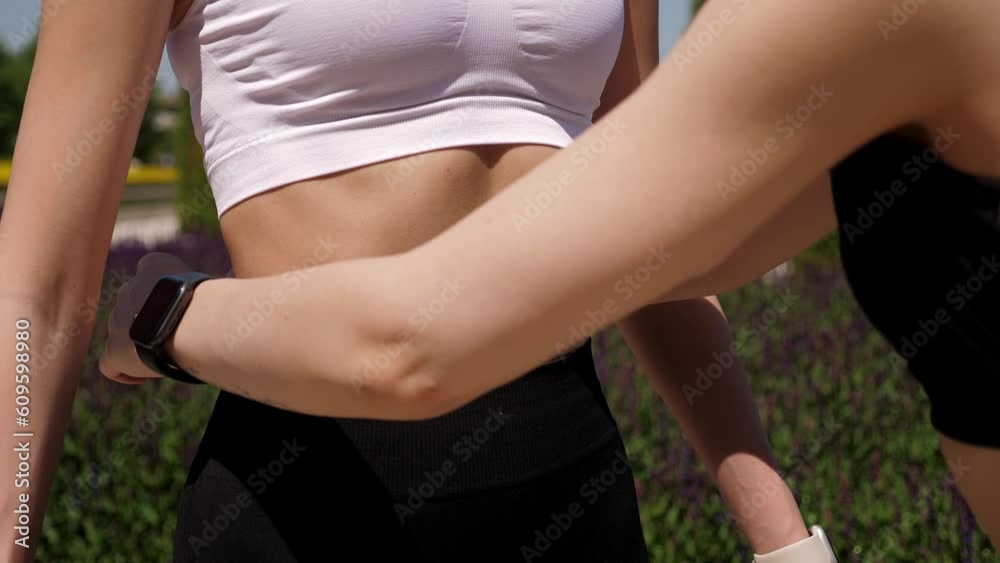 A close-up of a trainer measuring the waist of a young slender woman with a measuring tape in a park in summer. A close-up of a trainer measuring the waist of a young slender woman with a measuring tape in a park in summer.