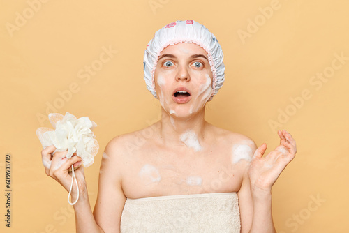 Fényképezés Shocked astonished surprised female dressed bath cap looking at camera with open mouth holding sponge with foam taking shower in thew morning expressing fear