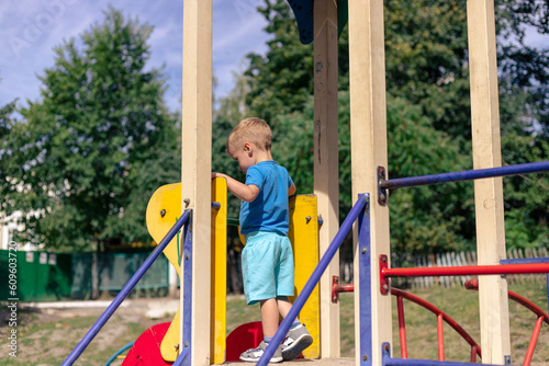 A little boy is playing on the playground. The boy on the child's slide