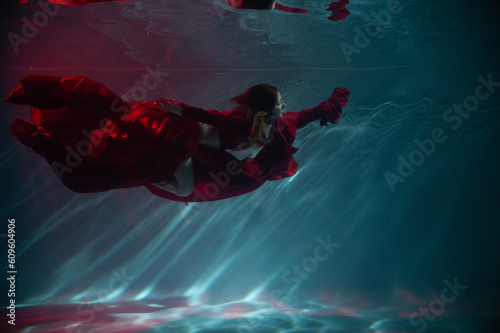 a girl under water, in an aquarium, in a pool in a red long dress swims like a mermaid