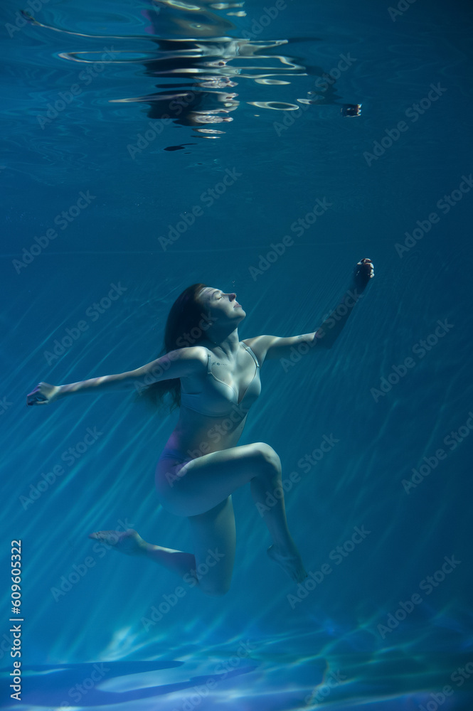 a girl under water, in an aquarium, in a pool in flesh-colored underwear naked swims like a mermaid